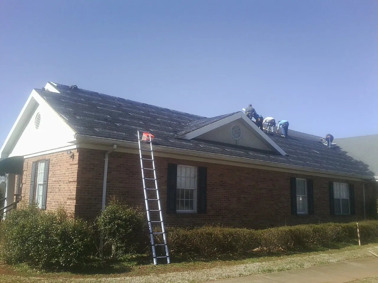 Crew tearing shingles off a brick ranch roof with a ladder set — Emergency Roof Repair work by our crew in Elwood
