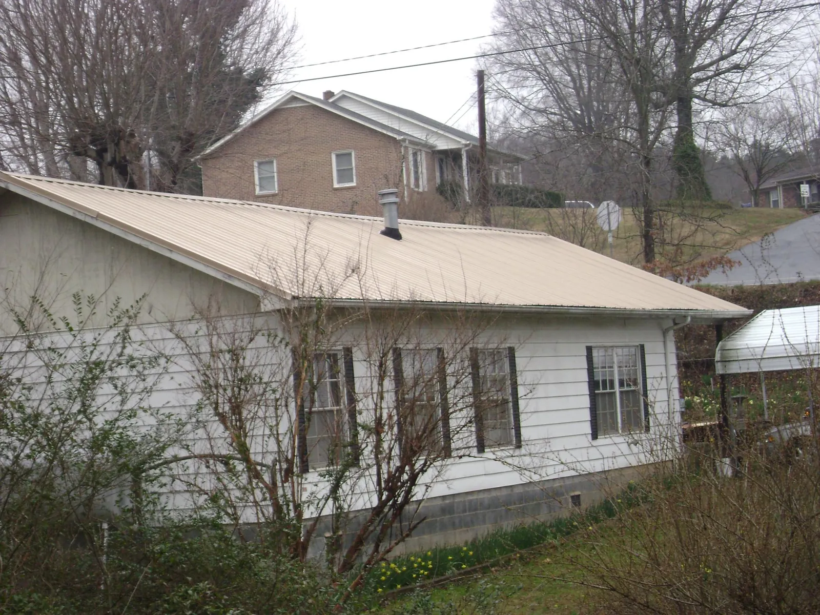 Tan metal roof on a white sided house set into a hillside — Commercial Roofing by Roofing Brothers in Elwood