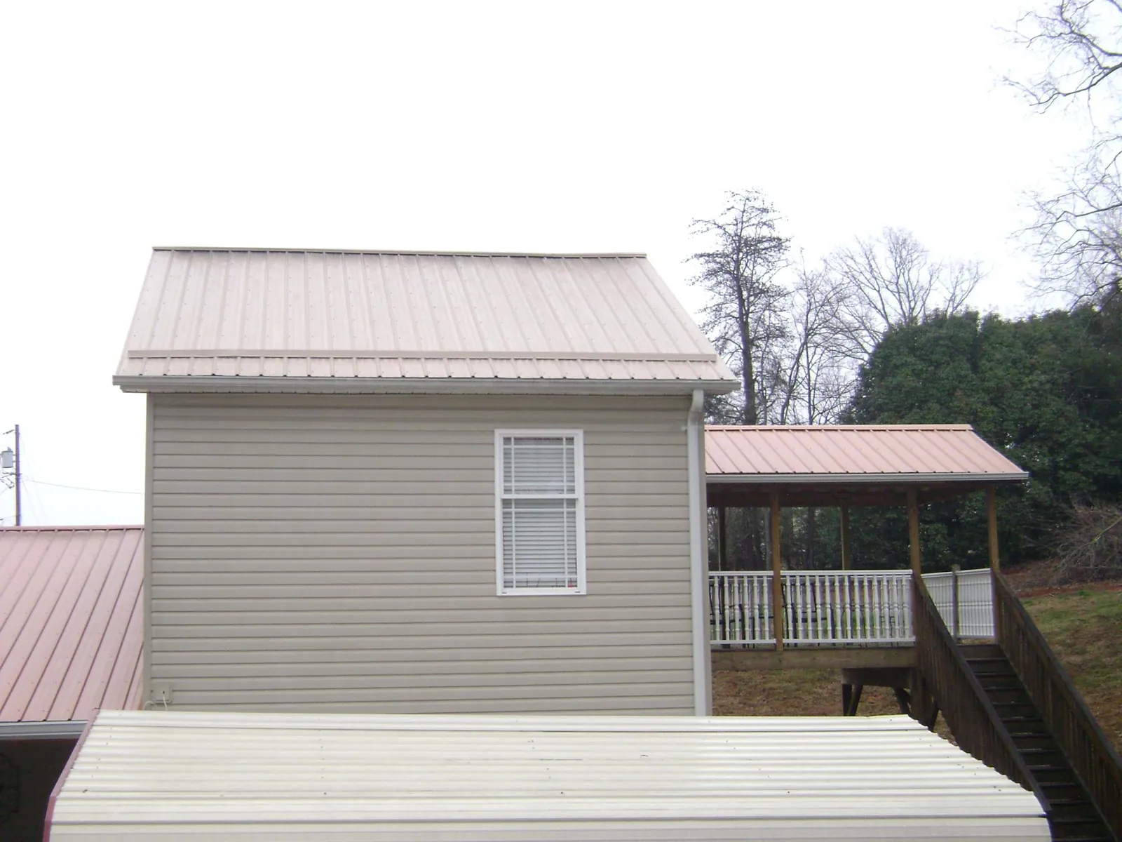 Tan metal roofs on a two story addition and attached porch, from a Roof Replacement job in Elwood